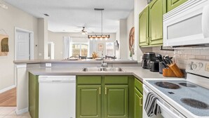 Una cocina con armarios verdes, un lavavajillas blanco, una estufa y un fregadero.