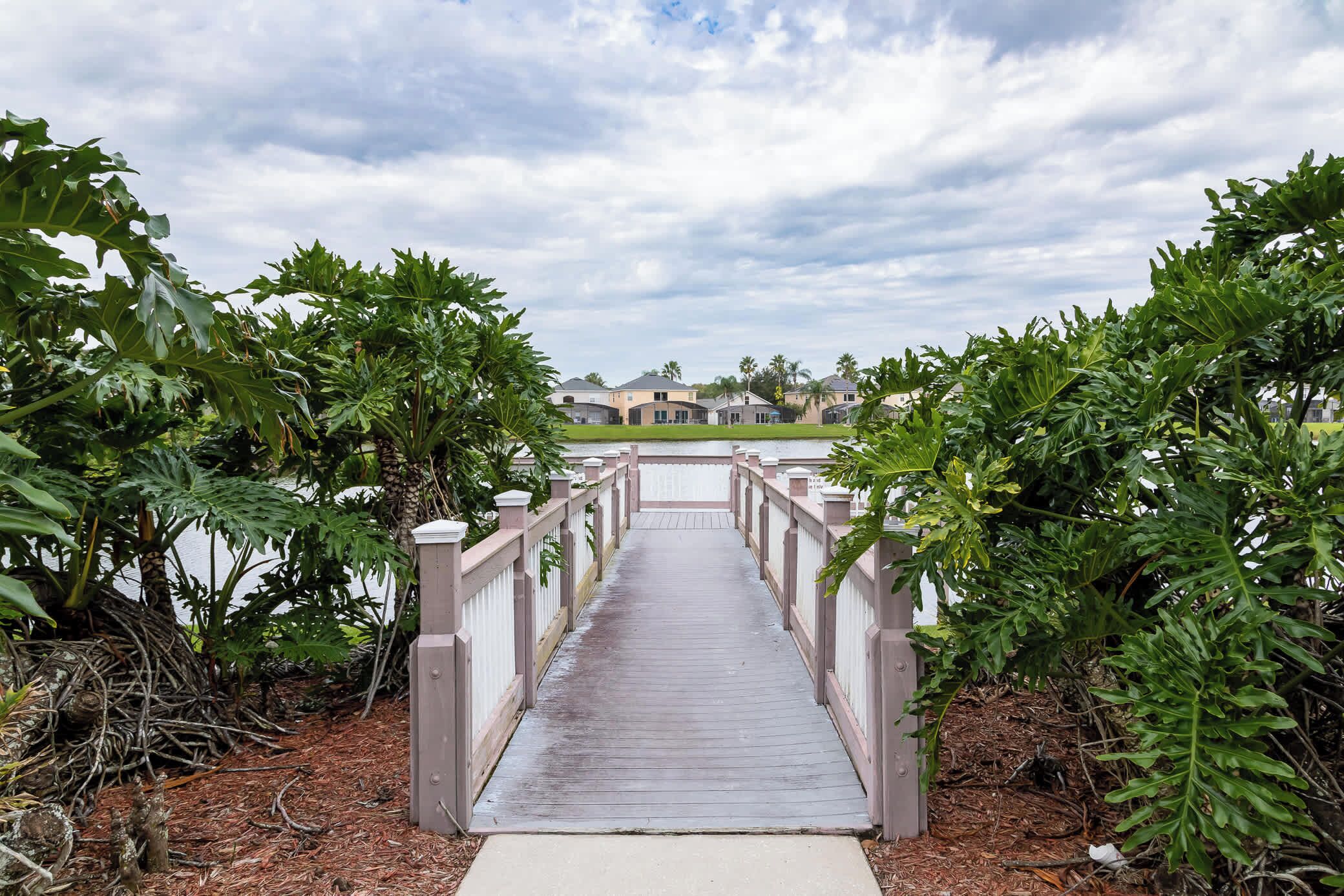 A wooden bridge leading to a row of houses with a cloudy sky above.