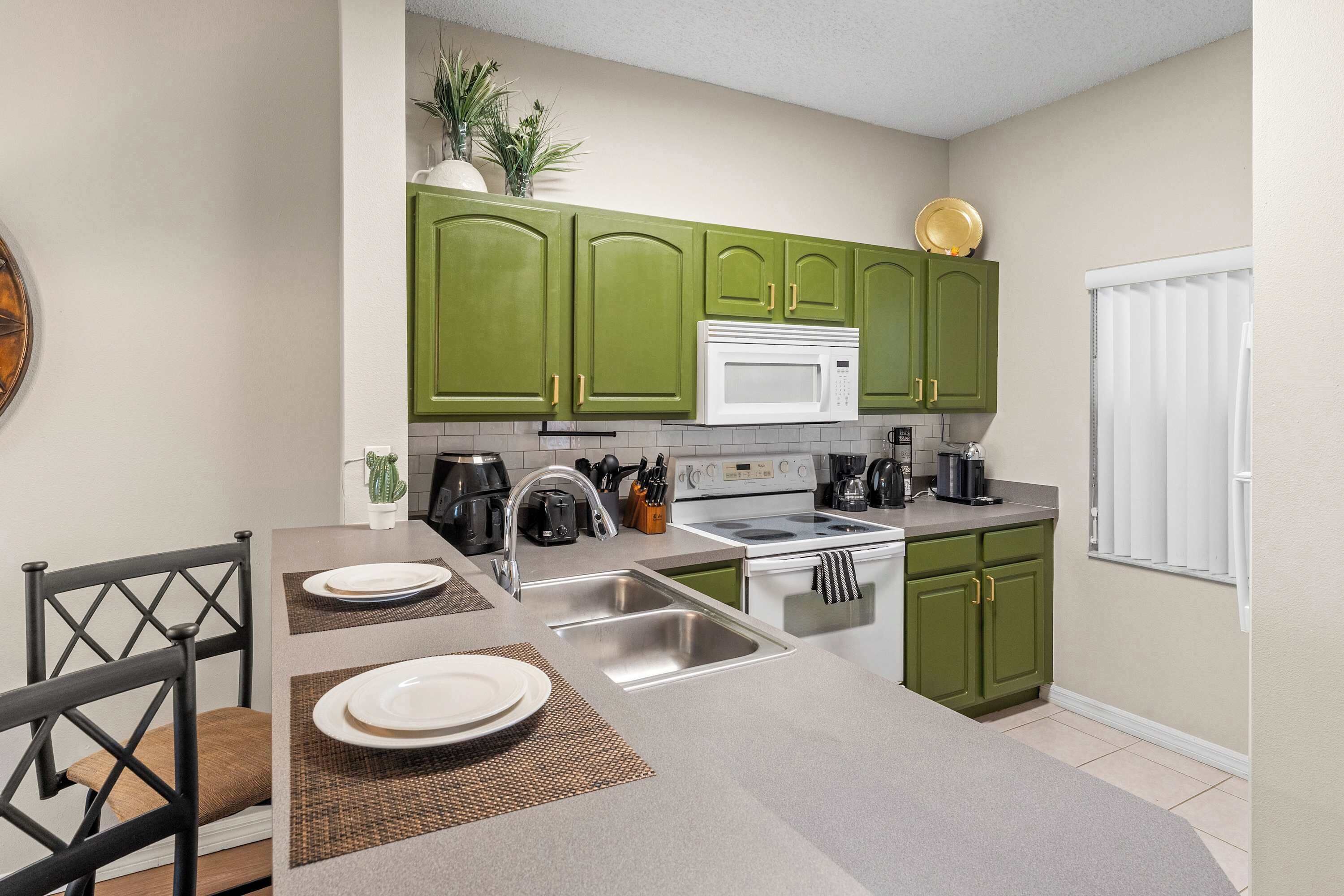 Een moderne keuken met groene kastjes, een witte magnetron en een RVS spoelbak.