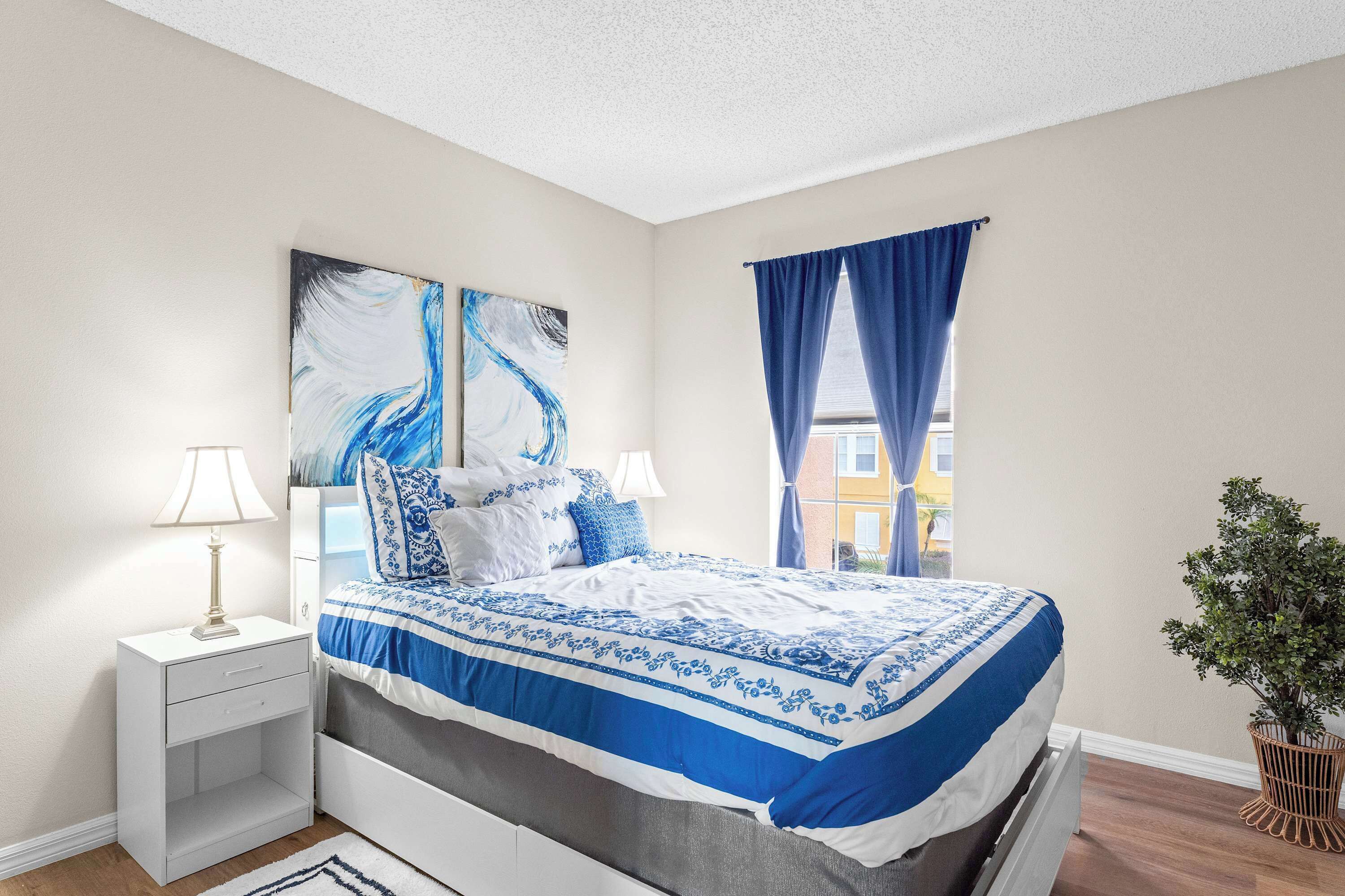 A bedroom with a bed, nightstand, lamp, and a large abstract painting on the wall.