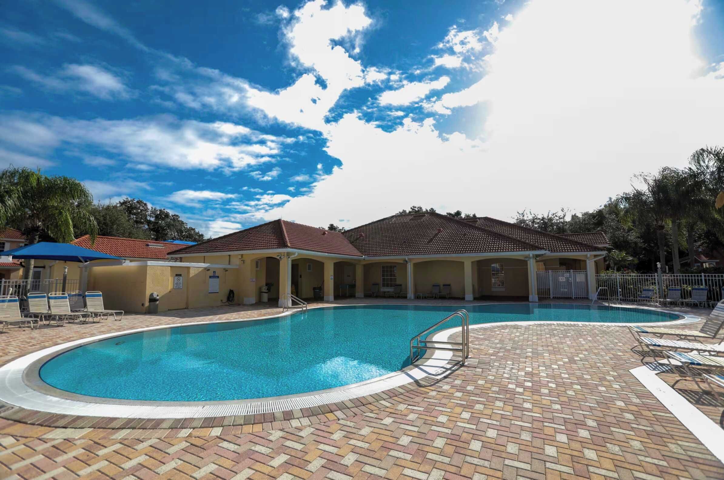 Una piscina con solárium de baldosas, sillas de descanso y un pabellón cubierto.