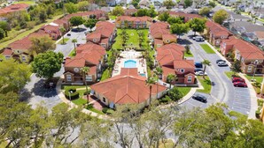 Un barrio residencial con varias casas de dos pisos, una piscina central y un lago al fondo.