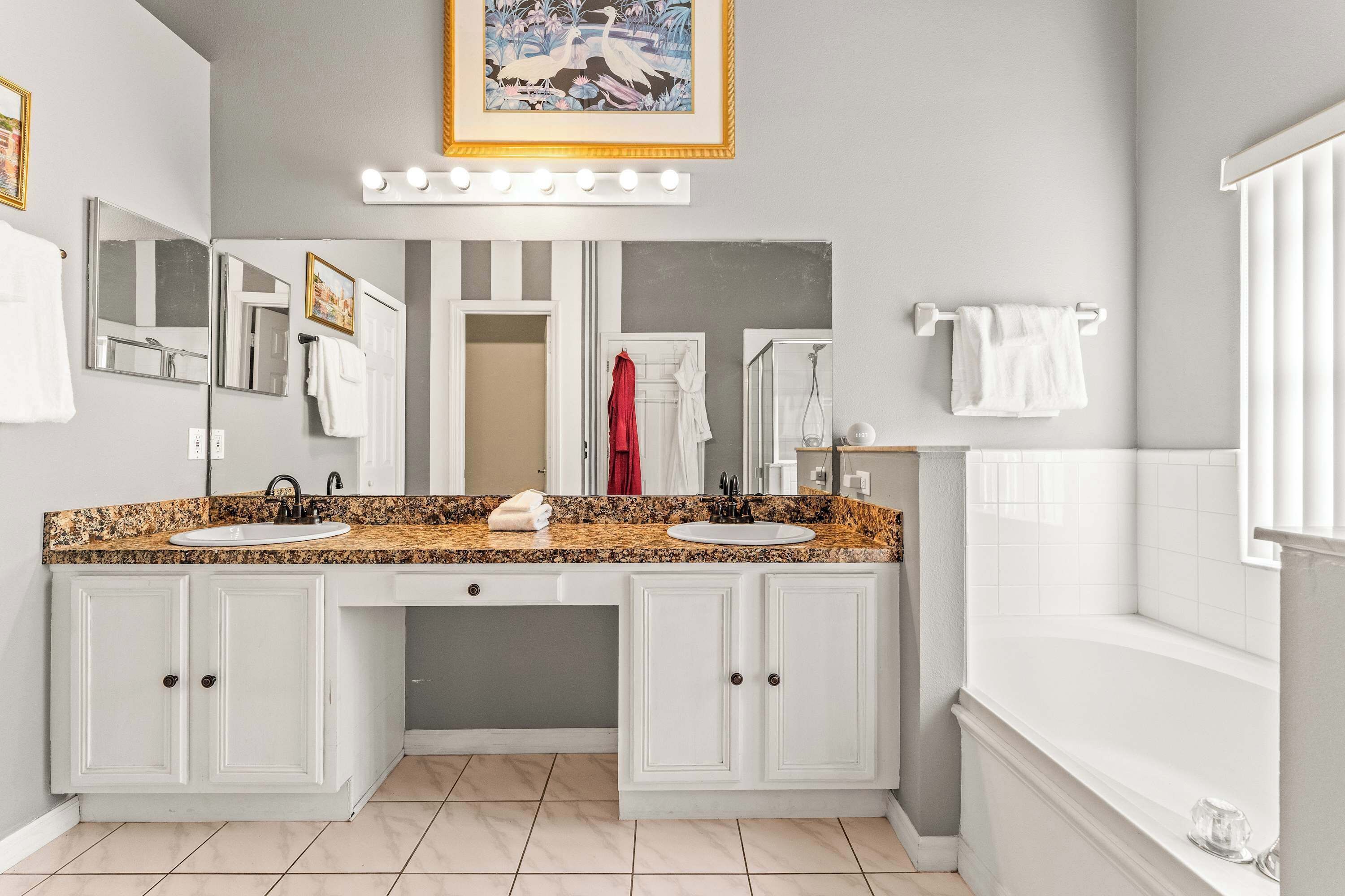 A bathroom with a double sink vanity, a large mirror, and a bathtub.