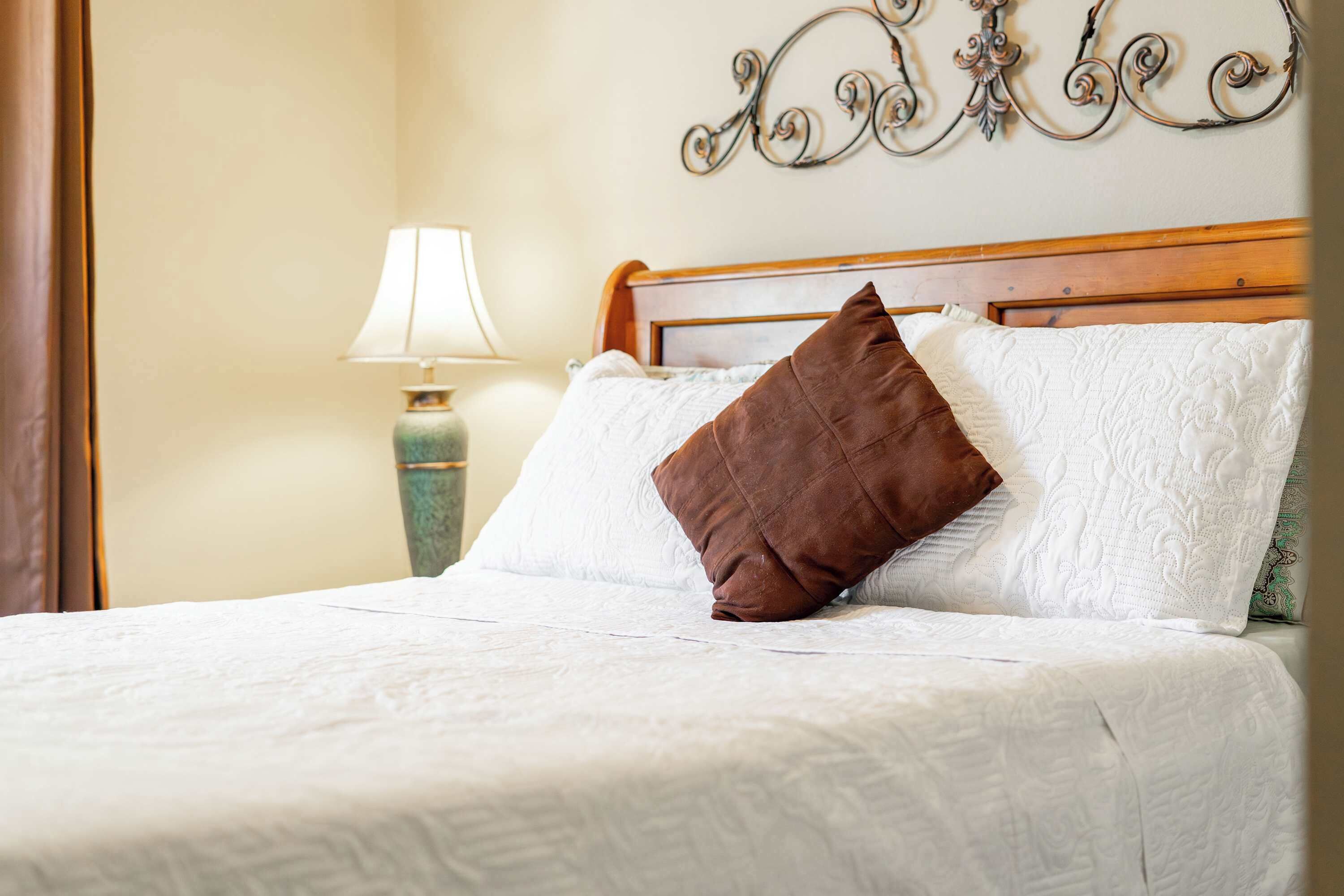 A neatly made bed with white linens and a brown pillow, a bedside lamp, and a decorative wall piece.