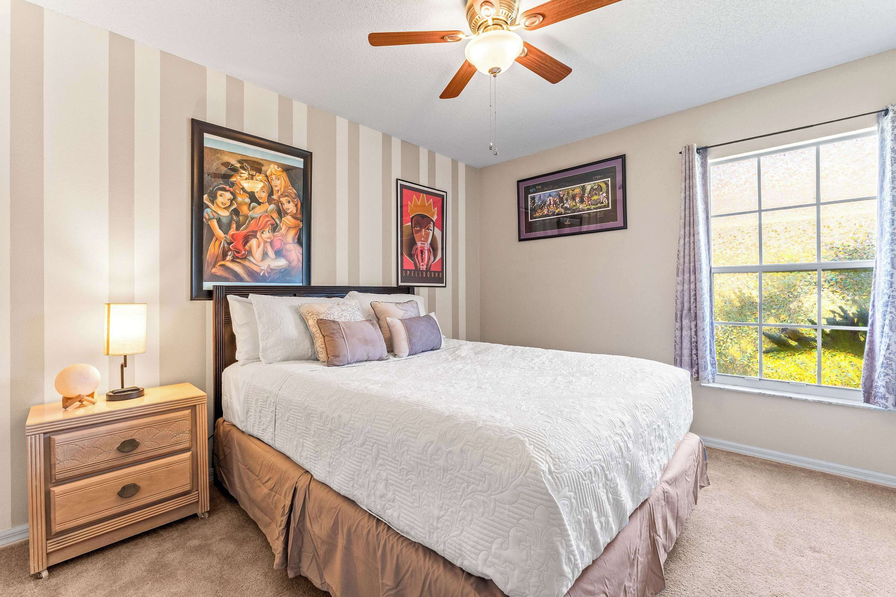 A bedroom with a bed, a nightstand, a ceiling fan, and two framed pictures on the wall.