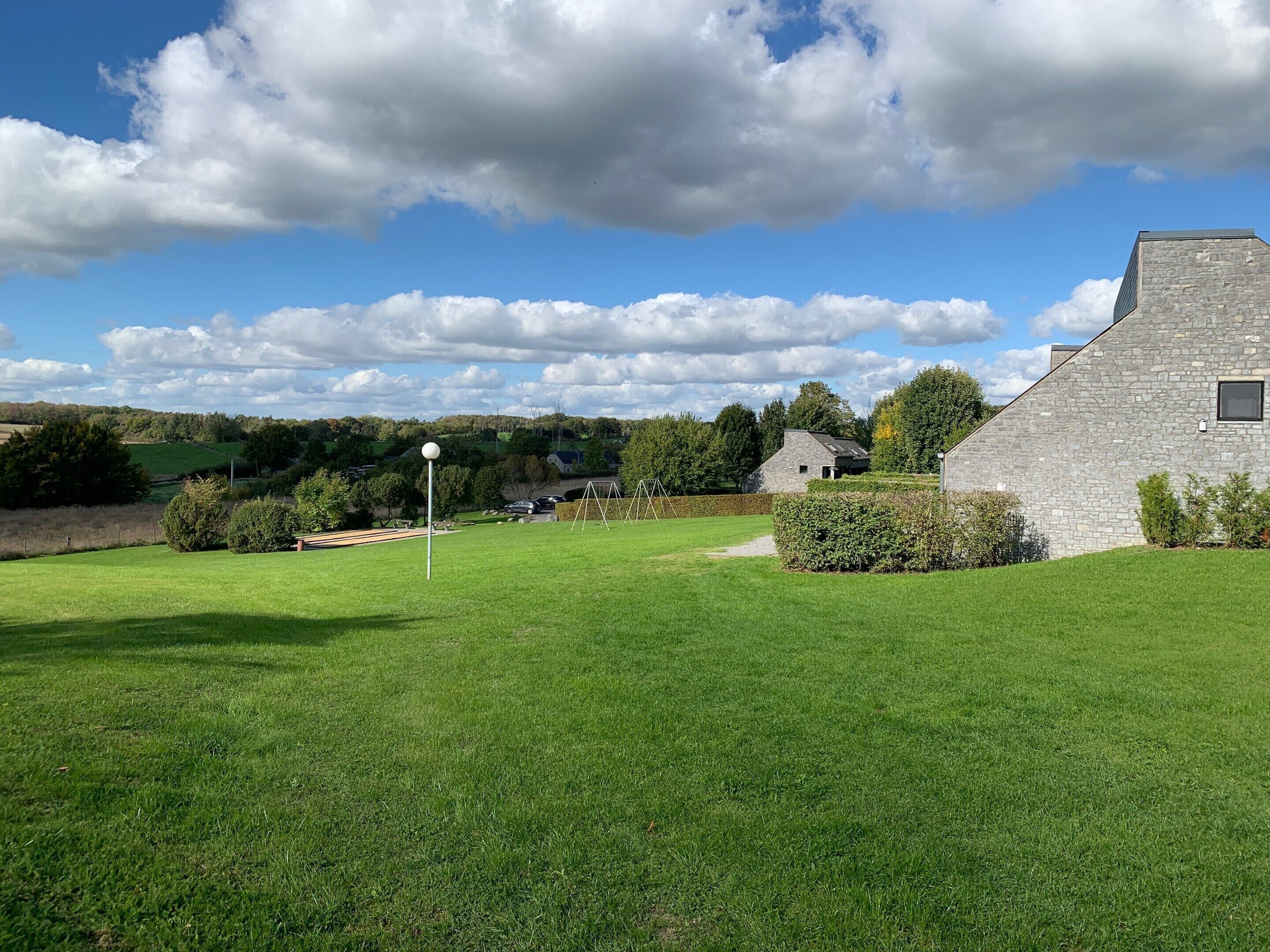 Eine grüne Wiese mit einem Steinhaus, einer Schaukel und einem Fahnenmast.