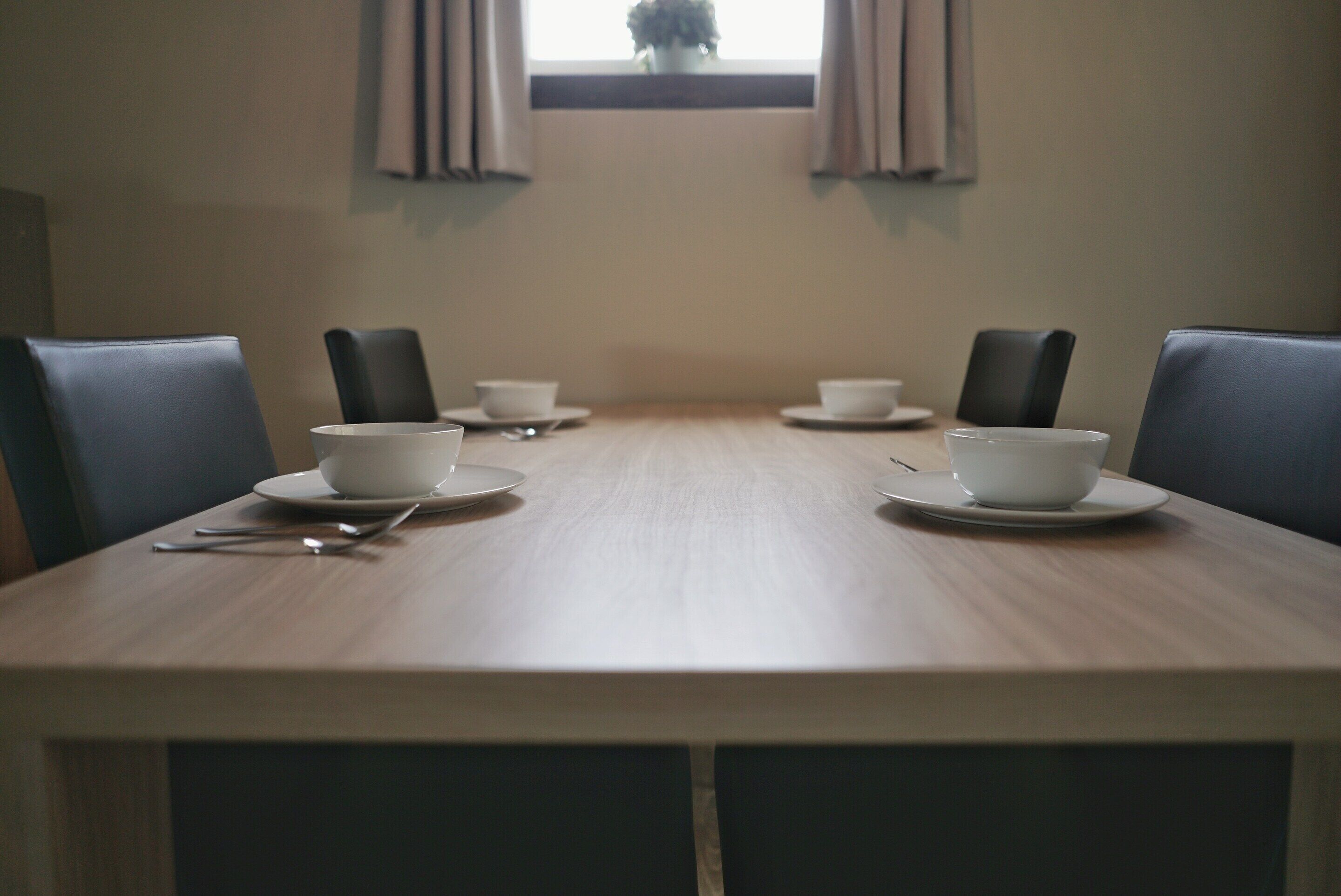 Une salle de conférence avec une longue table, quatre chaises et quatre tasses blanches posées sur des soucoupes.