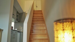 Un escalier menant à un deuxième étage, avec un coin cuisine sur la gauche et un luminaire sur la droite.