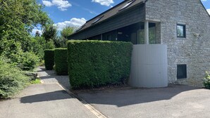 Un bâtiment en pierre avec un toit en pente, une allée gravillonnée et des haies soigneusement taillées.