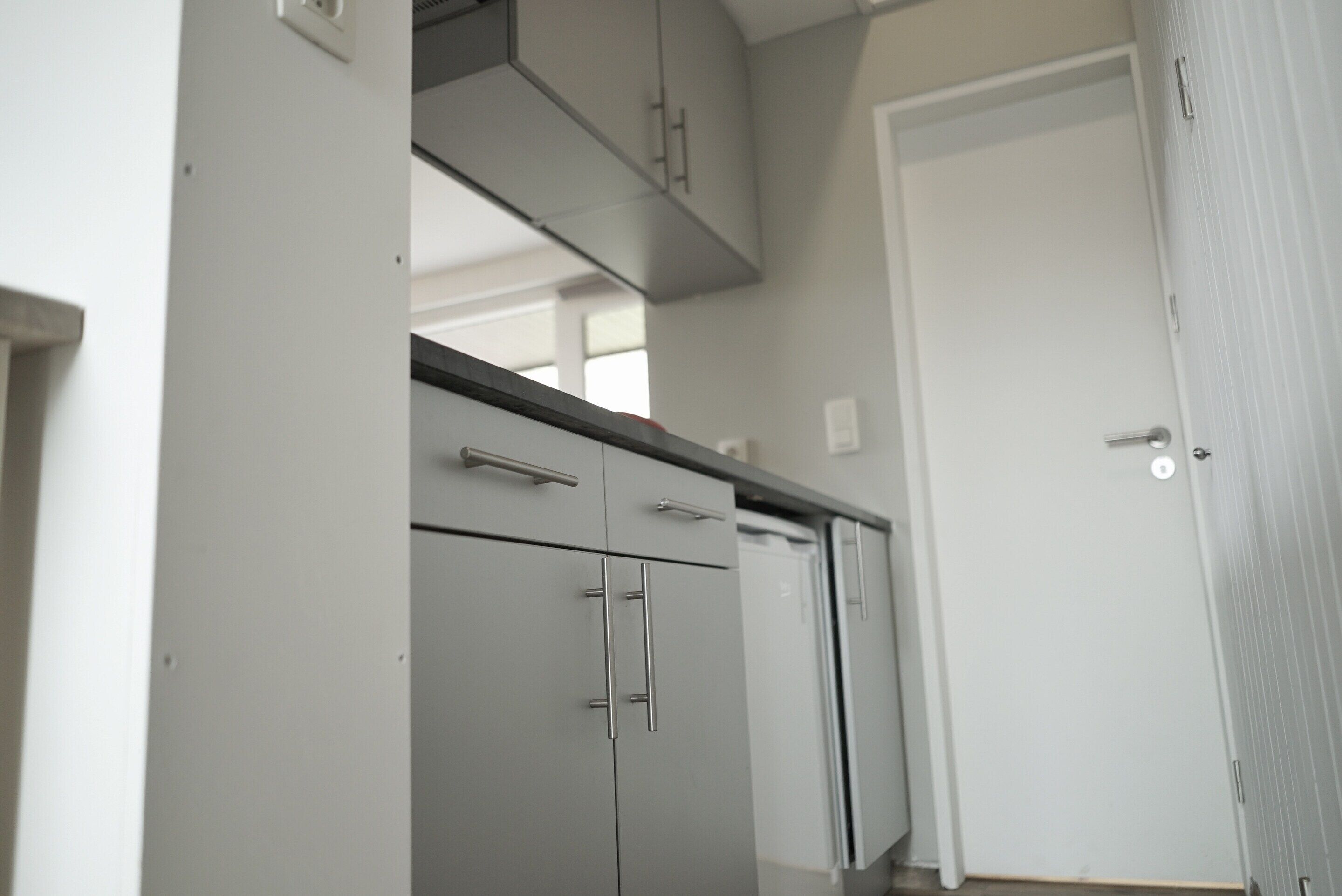 Una cocina con gabinetes grises, una puerta blanca y una ventana al fondo.