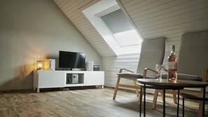 Un salon moderne doté d’un plafond en pente, d’un téléviseur à écran plat, d’un meuble de rangement blanc, d’une table basse ronde et d’un coin repas avec une chaise.