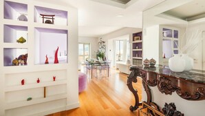 Ein geräumiges Zimmer mit Holzboden, einem Essbereich mit Glastisch und einem großen Spiegel an der Wand.