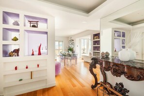 Ein geräumiges Zimmer mit Holzboden, einem Essbereich mit Glastisch und einem großen Spiegel an der Wand.