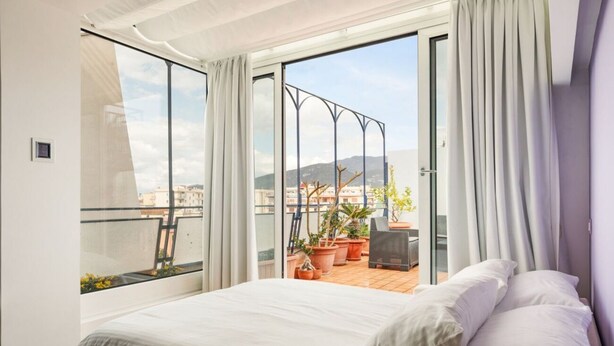 Ein Schlafzimmer mit großem Fenster, einem Balkon mit Blumentöpfen und einem Bett mit weißer Bettwäsche.
