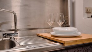 A stainless steel kitchen sink with a modern faucet, a wooden cutting board, and a stack of white plates and two wine glasses. - Hostmate - Milano - Pontaccio - Brera (Milano)