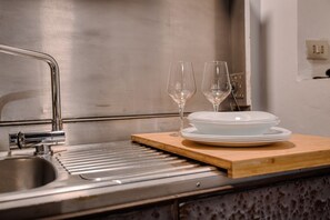 A stainless steel kitchen sink with a modern faucet, a wooden cutting board, and a stack of white plates and two wine glasses. - Hostmate - Milano - Pontaccio - Brera (Milano)