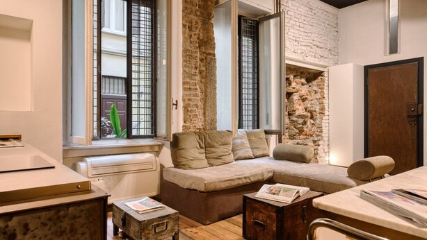 A cozy living room with a stone wall, a sofa, a coffee table, and a window with a view. - Hostmate - Milano - Pontaccio - Brera (Milano)