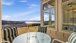 A glass-top table with two bottles, a striped sofa, and a large window offering a view of a lake and houses. - Majestic Retreat Stay for 6 (Branson)