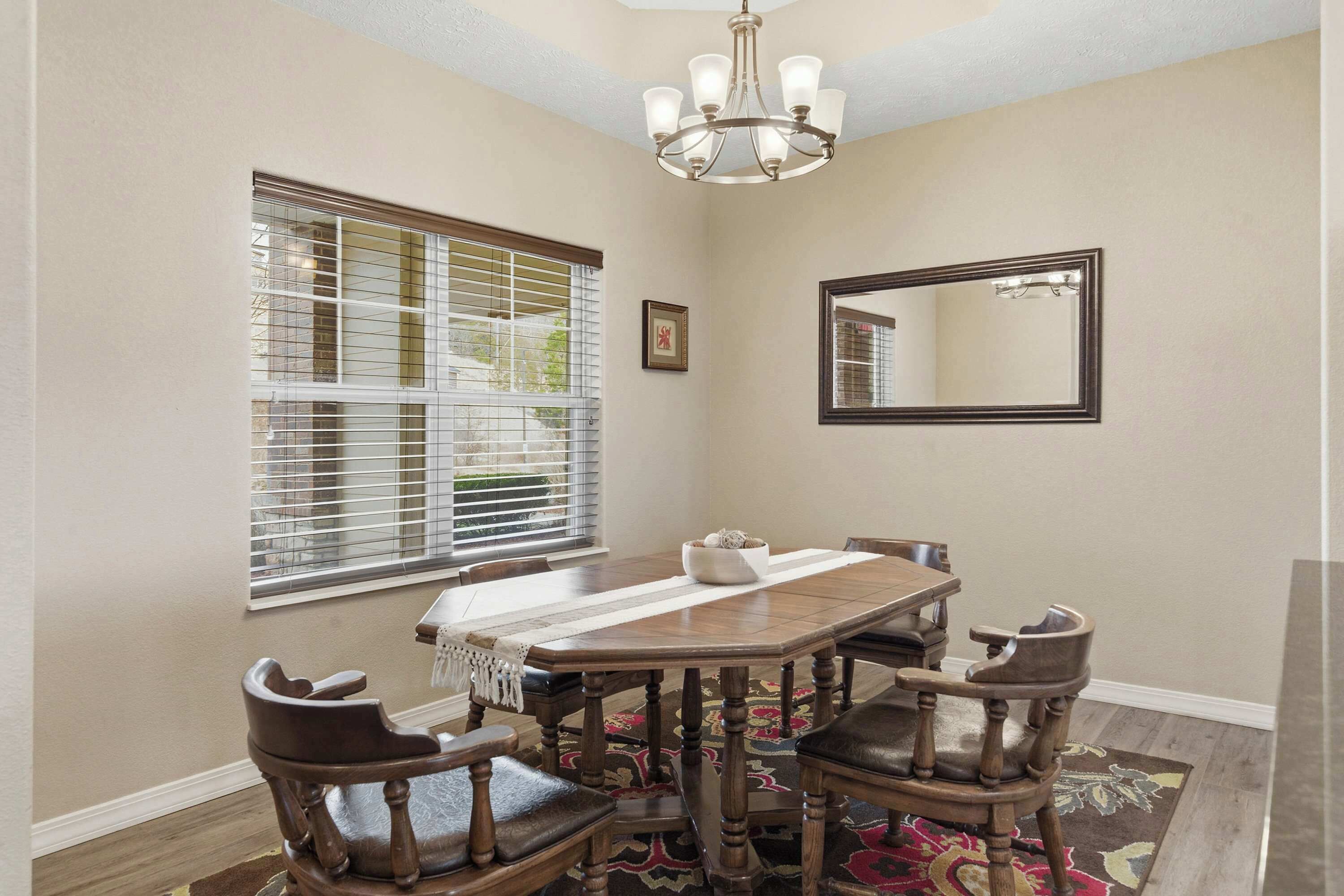 A dining room with a wooden table, chairs, a chandelier, and a window with blinds.