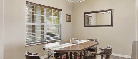 A dining room with a wooden table, chairs, a chandelier, and a window with blinds.