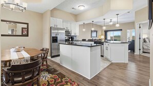 A spacious kitchen with white cabinetry, a central island, and a dining area with a wooden table and chairs. - Majestic Retreat Stay for 6 (Branson)