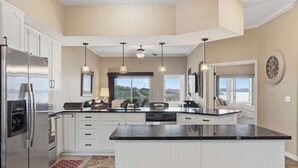 A modern kitchen with a large island, white cabinetry, stainless steel appliances, pendant lighting, and large windows offering a view of the outdoors. - Majestic Retreat Stay for 6 (Branson)