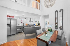 A modern kitchen with a central island, stainless steel appliances, and a dining area with a wooden table and grey upholstered chairs. - Rare Downtown Oasis | Private Pool + Parking (St. Augustine)