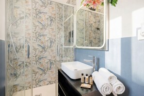 Un baño con papel tapiz floral, un lavabo blanco, un espejo y una ducha.