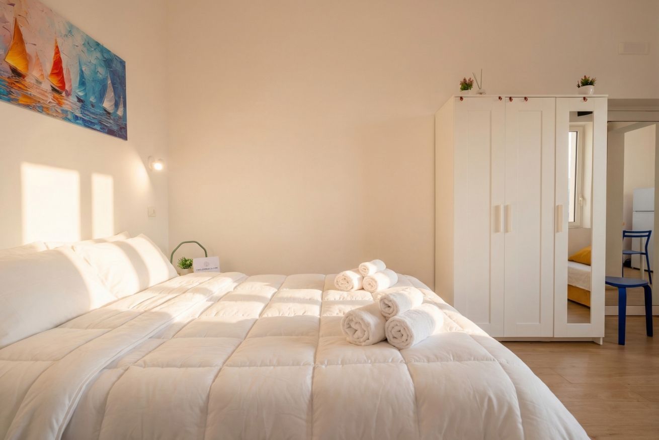 Una cama bien hecha con toallas enrolladas, un armario blanco y un cuadro en la pared.