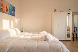 A neatly made bed with rolled towels, a white wardrobe, and a painting on the wall. - Blu Mediterraneo - Comfortable Apartment Near the Sea (Bari)