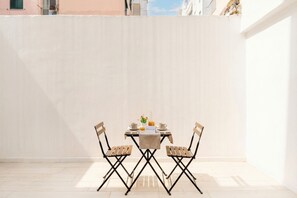 Una mesa de comedor con sillas en un patio al aire libre, con una pared blanca y vistas a edificios en la distancia.