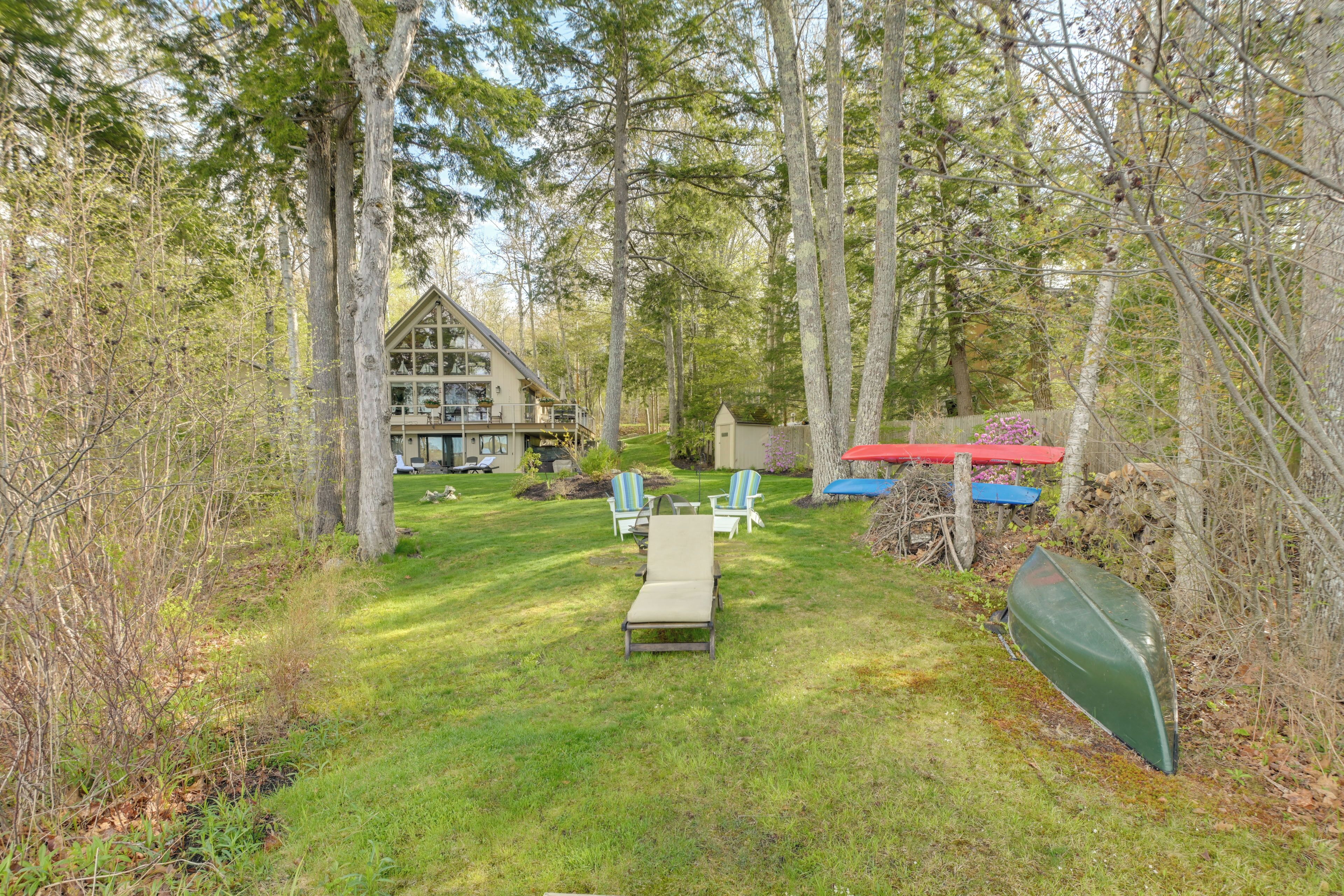 A cabin with a deck, surrounded by trees, and a grassy yard with outdoor furniture.