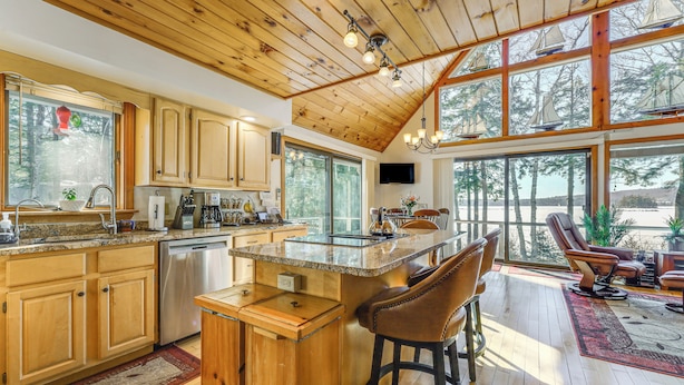 Una cocina amplia con armarios de madera, una isla grande con taburetes de bar y un comedor con vistas al exterior.