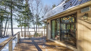 Una terraza de madera cubierta de nieve con un ventanal que da a una habitación.