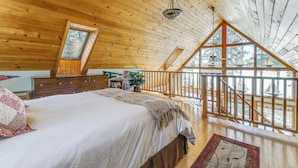 Un dormitorio con una cama grande, techo de madera, una ventana y un balcón con barandilla.