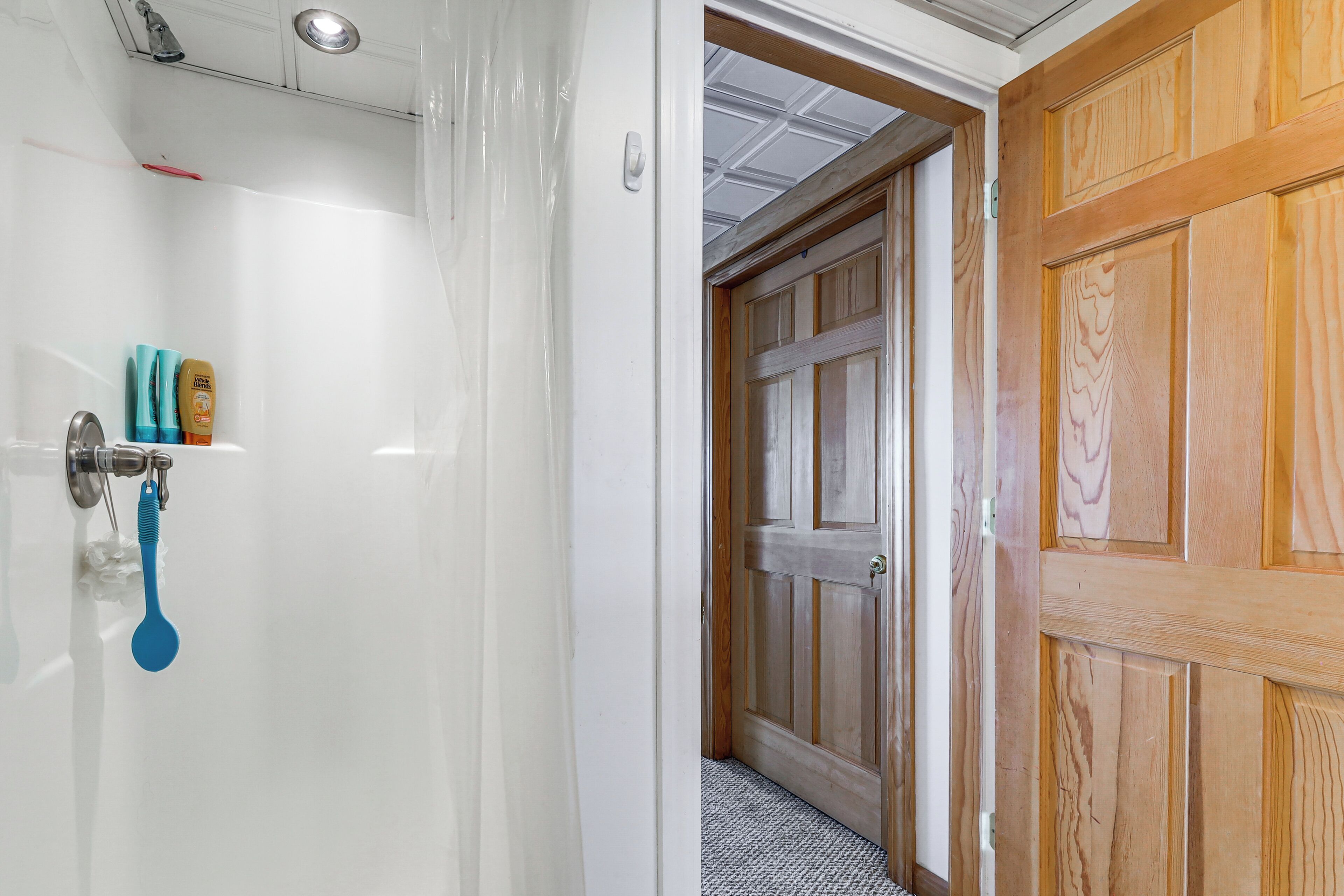 Un baño con pared blanca, ducha y cabezal de ducha azul.