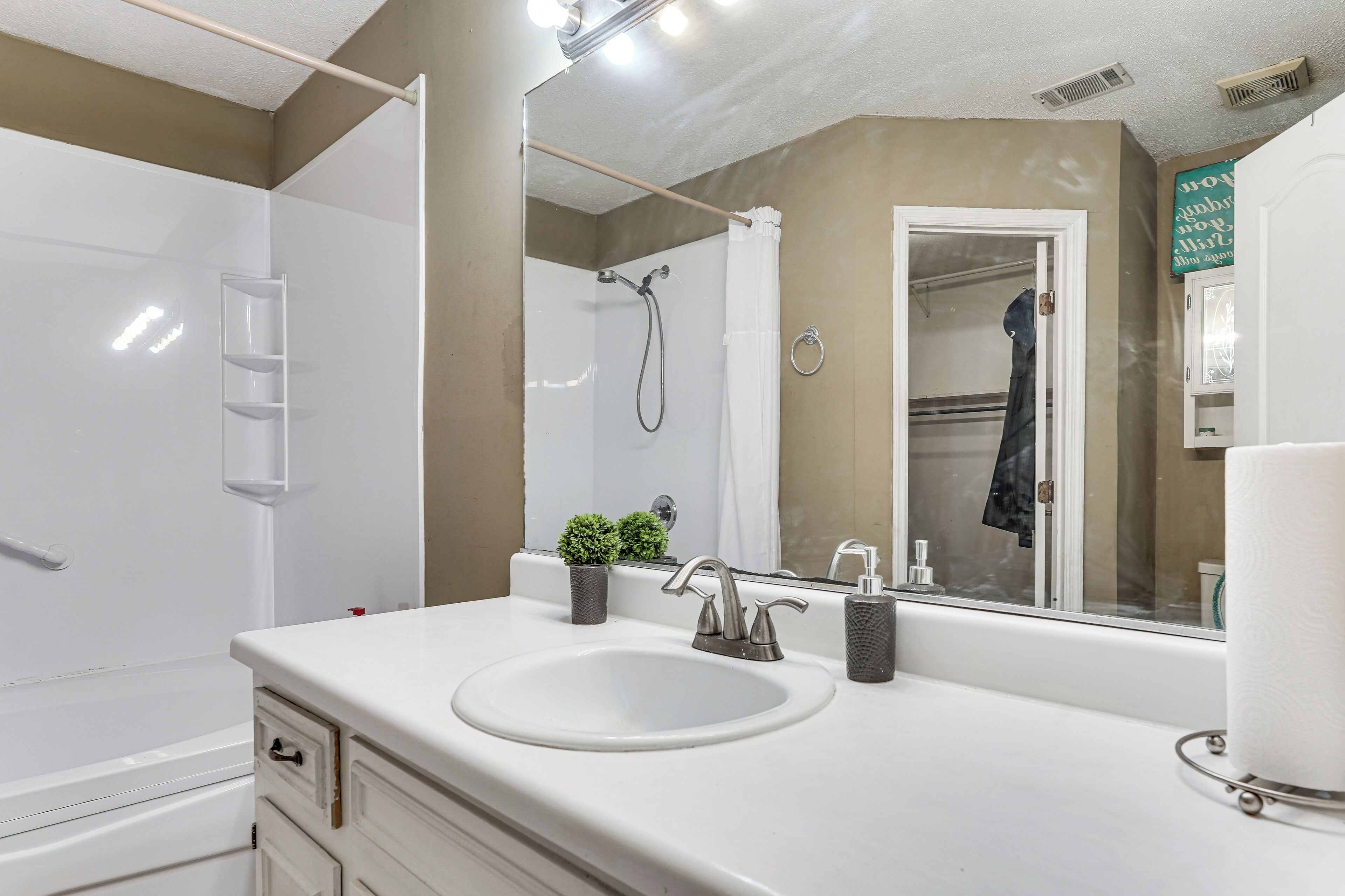 Un baño moderno con un lavamanos blanco, un espejo grande, una ducha y un perchero para toallas.