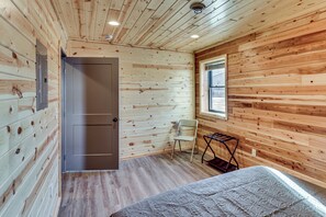 A wooden-paneled room with a bed, a chair, a window, and a door. - 2 Mi to Lake Traverse: Dog-friendly Getaway (Browns Valley)