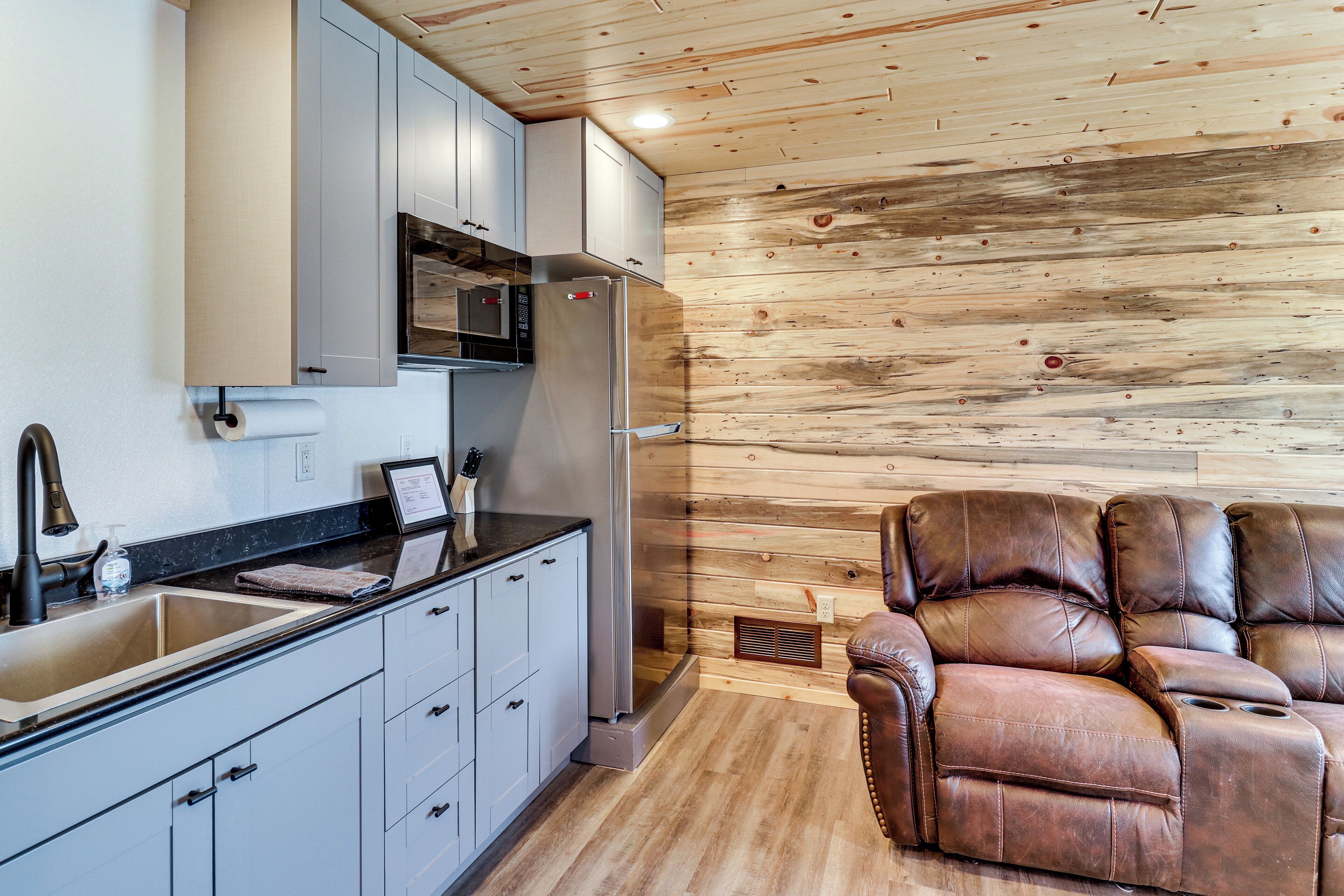 A modern kitchen with stainless steel appliances, a built-in oven, and a large sink. There is a leather sofa with a reclining feature in the living area.