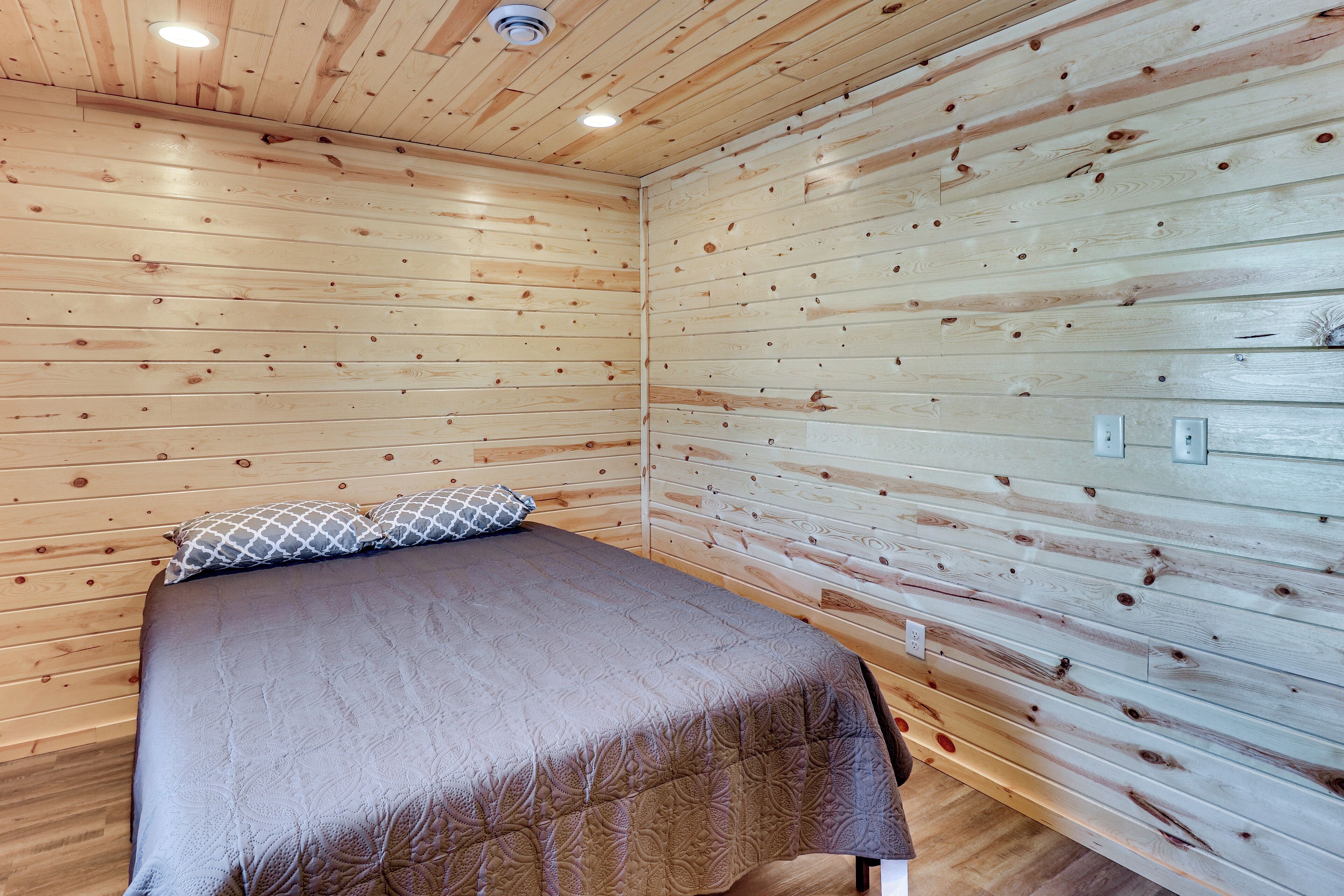 A room with wooden panel walls, a bed with a patterned bedspread, and a ceiling light.