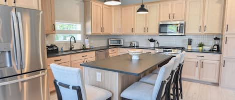 Una cocina moderna con armarios de madera, electrodomésticos de acero inoxidable y una isla central con taburetes de bar.