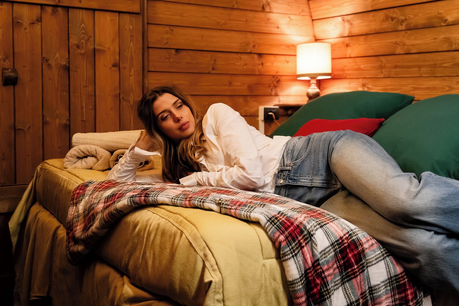 Una persona acostada en una cama en una habitación con paredes de madera y una lámpara en la esquina.