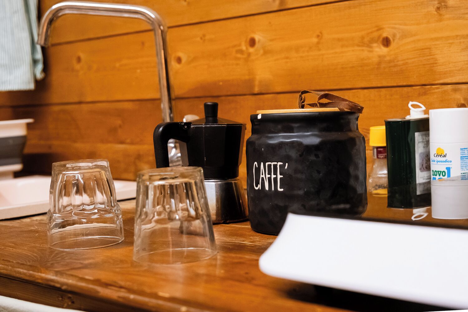 A kitchen counter with a coffee maker, a jar labeled "CAFFE'," and two glasses.