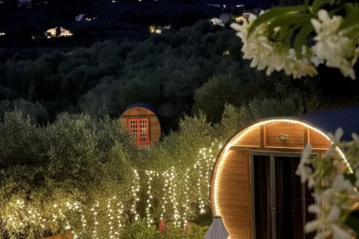 A wooden structure with a circular door, surrounded by a garden with string lights and a view of distant mountains.