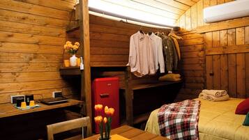 Un'accogliente camera da letto in legno, con un letto coperto da una coperta a quadri, un termosifone rosso e un tavolo con un vaso di fiori.