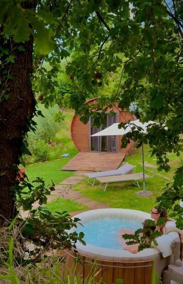 A hot tub surrounded by a wooden deck, a covered outdoor seating area, and a circular wooden structure. - LE BOTTI FIORENTINE (Reggello)
