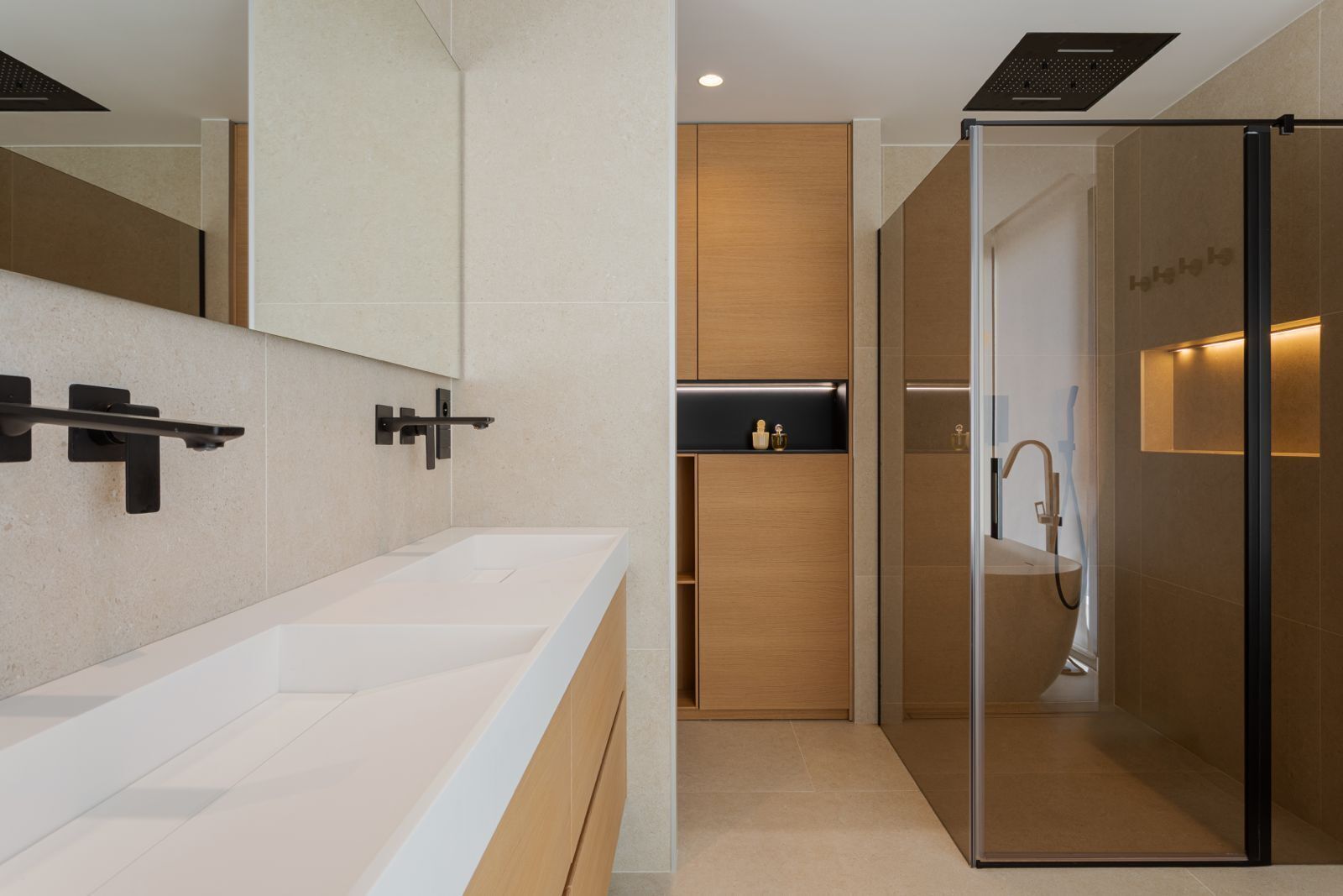 Une salle de bain moderne avec un grand miroir, deux lavabos, une douche et un espace douche fermé par des parois de verre.