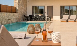 Un espace aménagé au bord de la piscine, avec des chaises longues, une table où sont servis des boissons et un mur en pierre.