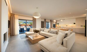 A modern living room with a sectional sofa, a coffee table, and a dining area with a kitchen in the background. - Sissi Lux Kappa Villa Private Pool (Sisi)