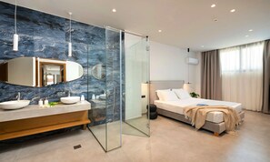 Una camera da letto moderna con cabina doccia in vetro, un letto grande con poggiatesta e un bagno con rivestimento in marmo e doppio lavabo.